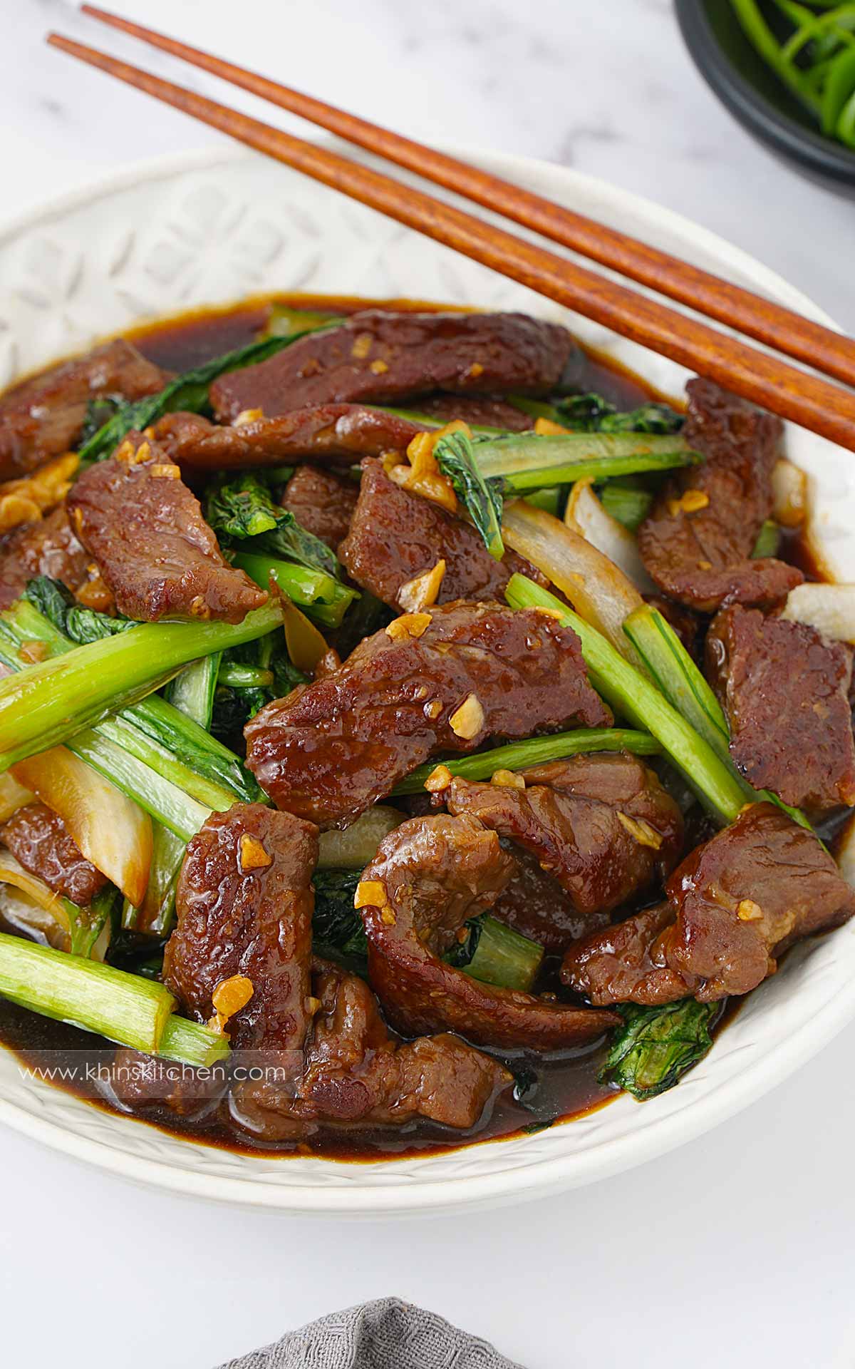 A white plate containing beef and green vegetables stir fry. Wooden chopstick at one side.