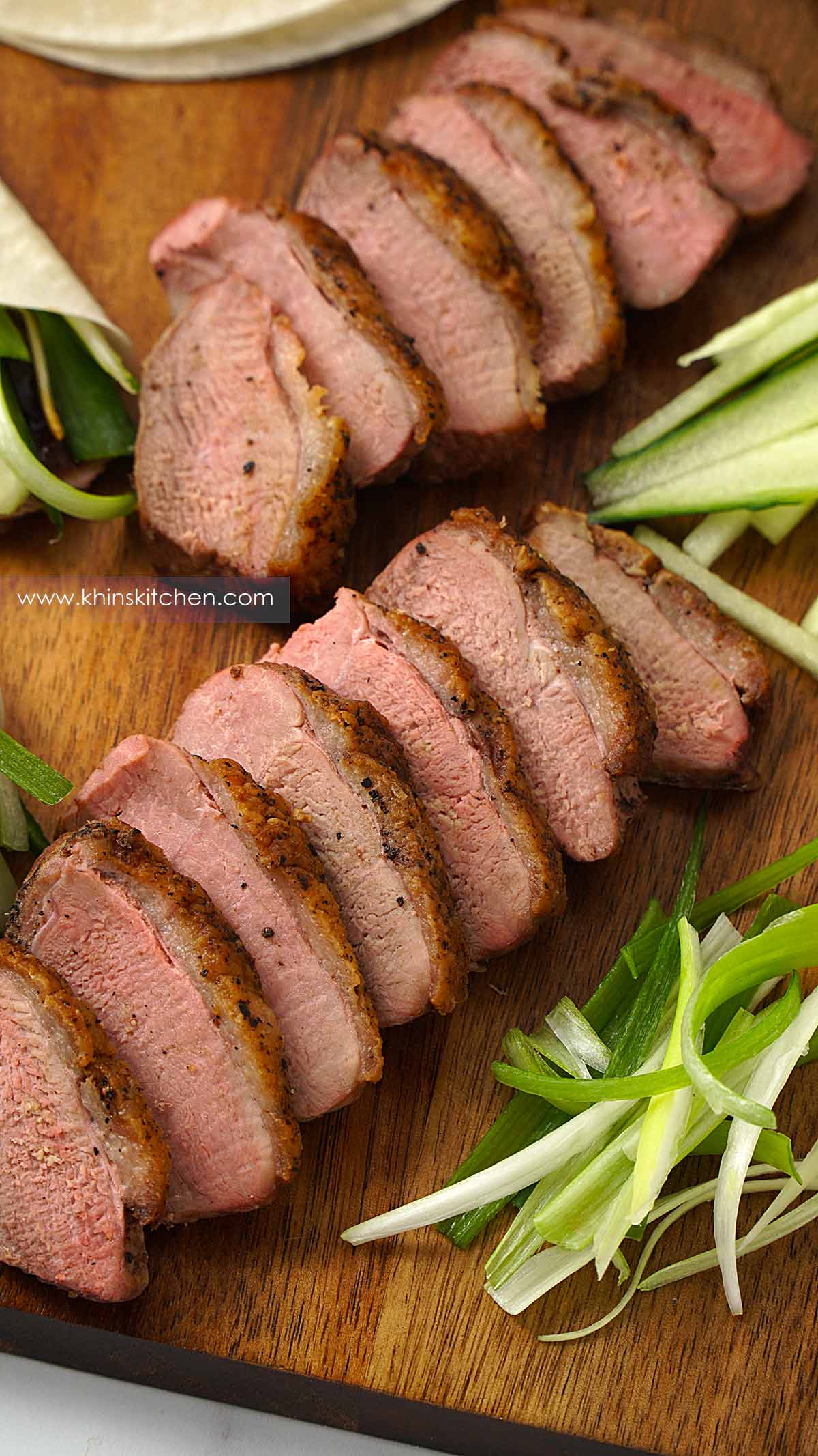 sliced duck, shredded spring onions, shredded cucumber and a white bowl of hoisin dipping sauce on the wooden serving board.