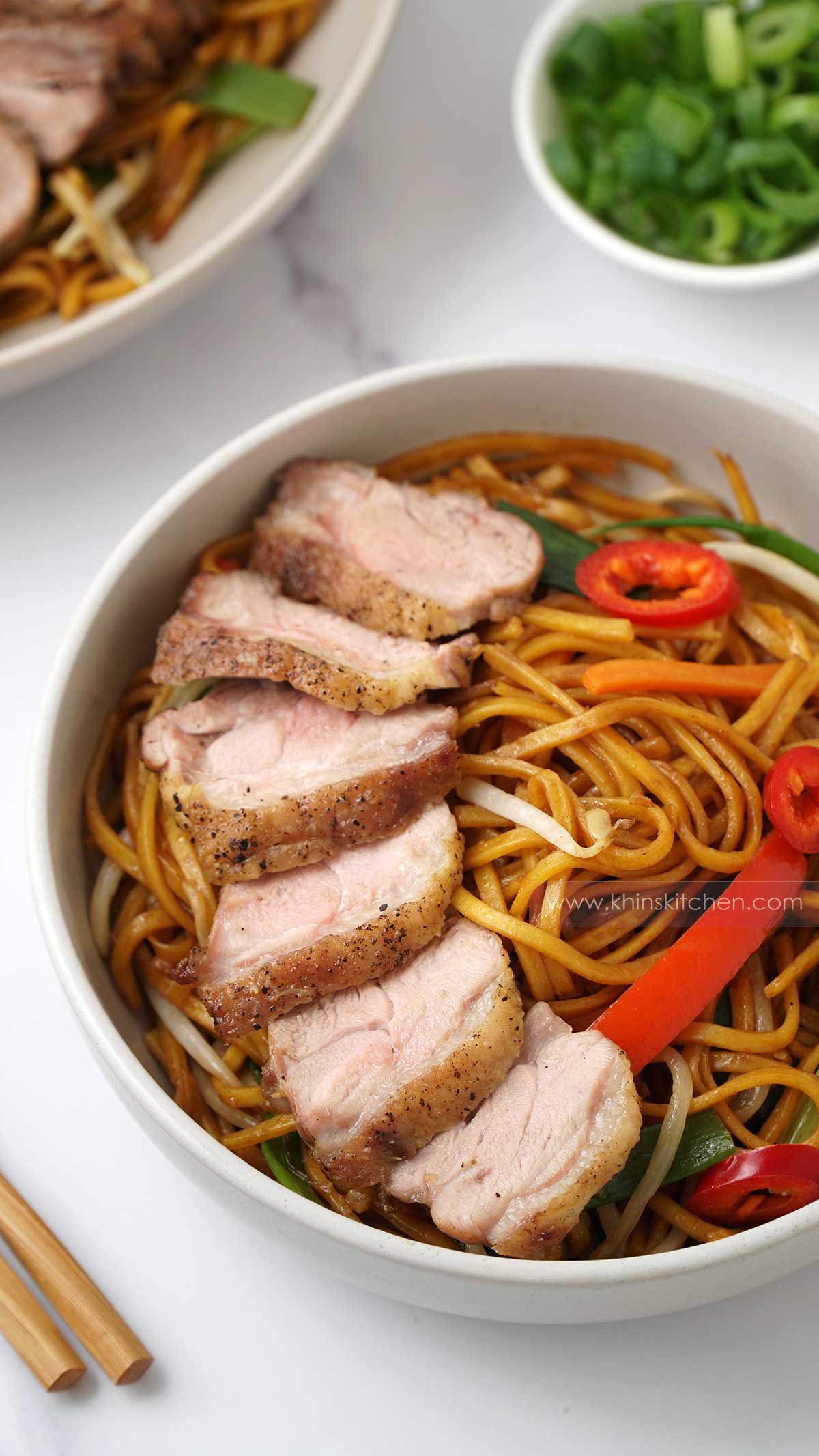 A white bowl containing stir fried noodles, vegetables and roasted sliced duck.