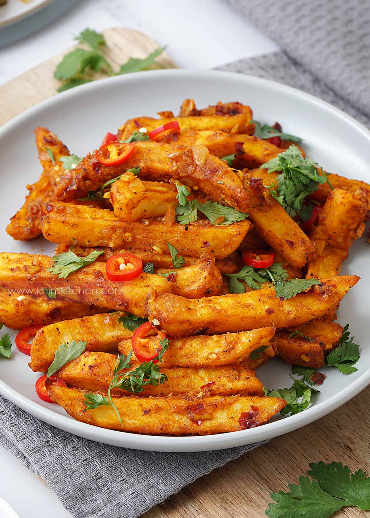 A grey plate containing crispy golden masala fries with coriander and red chilli slices. 