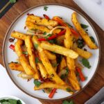 A white plate containing crispy fried chips and stir fried bell pepper sprinkle with coriander.