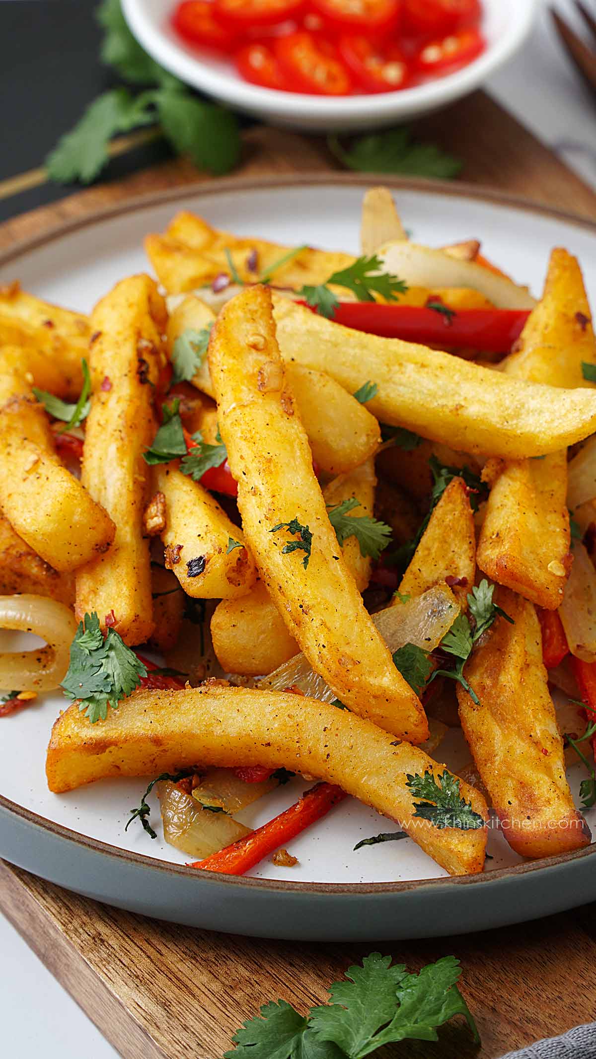 A white bowl containing chips, stir fried bell pepper with crushed chilli and sprinkle with chopped coriander.