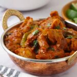 A steel bowl containing chicken curry and sprinkle with chopped coriander.