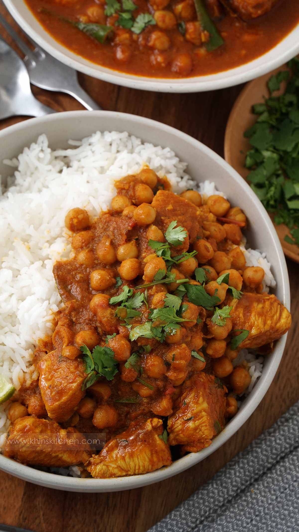 A grey bowl containing chicken curry with chick pea on top of the white rice.