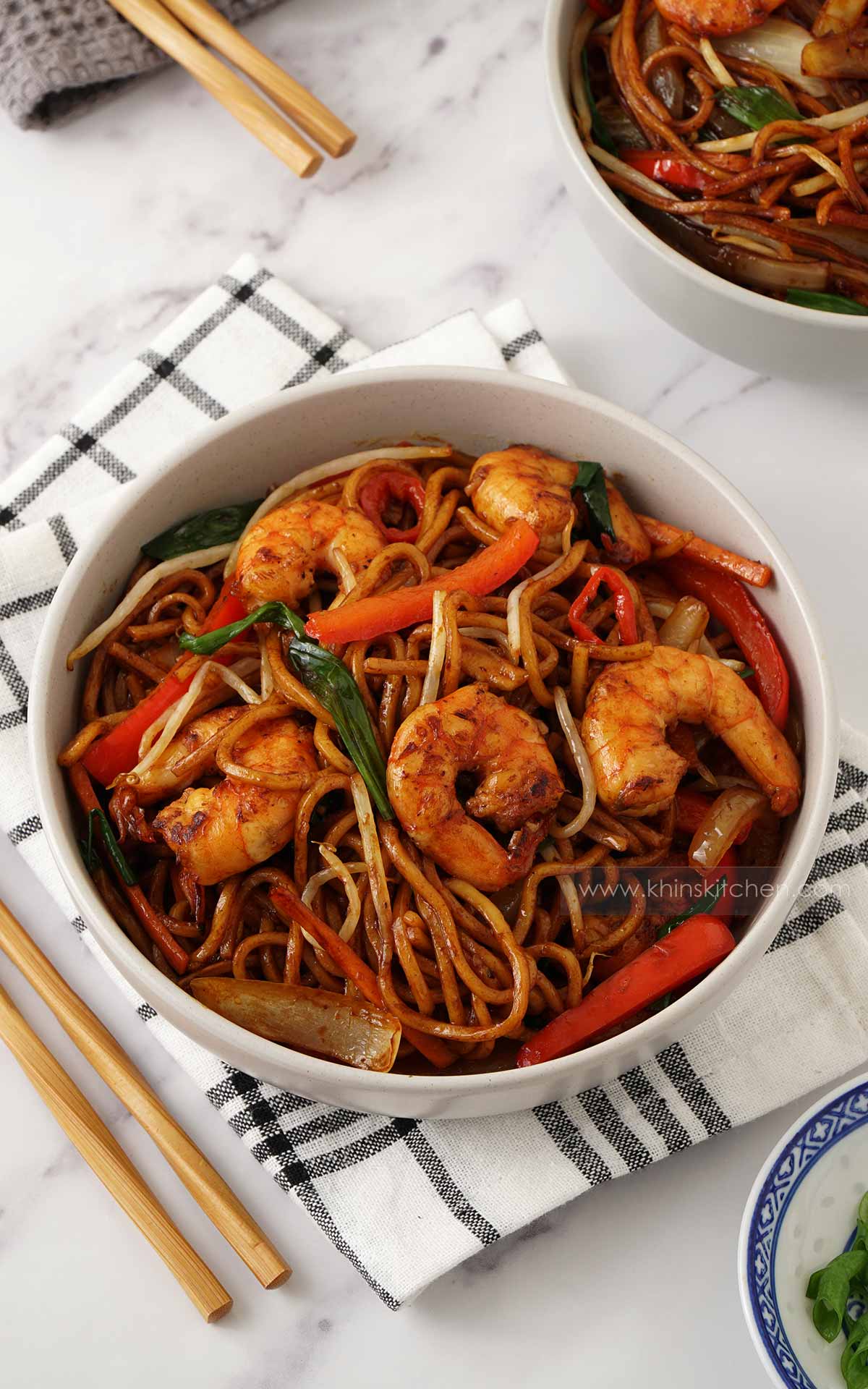 A white bowl containing stir fry noodles and prawns with vegetables, displayed on the white towel. 