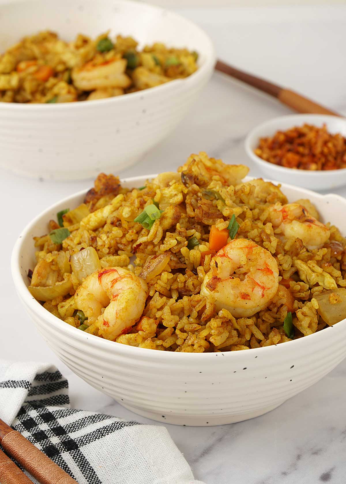 A white bowl containing fried rice, stir fried prawns, chickens and topped with spring onions.