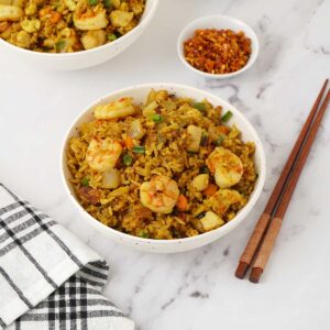 A white bowl containing fried rice with prawns, chicken and egg topped with chopped spring onions.
