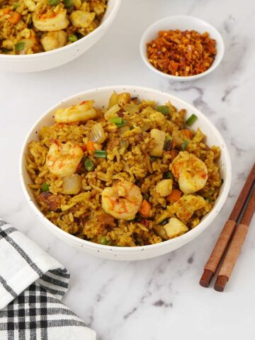 A white bowl containing fried rice with prawns, chicken and egg topped with chopped spring onions.
