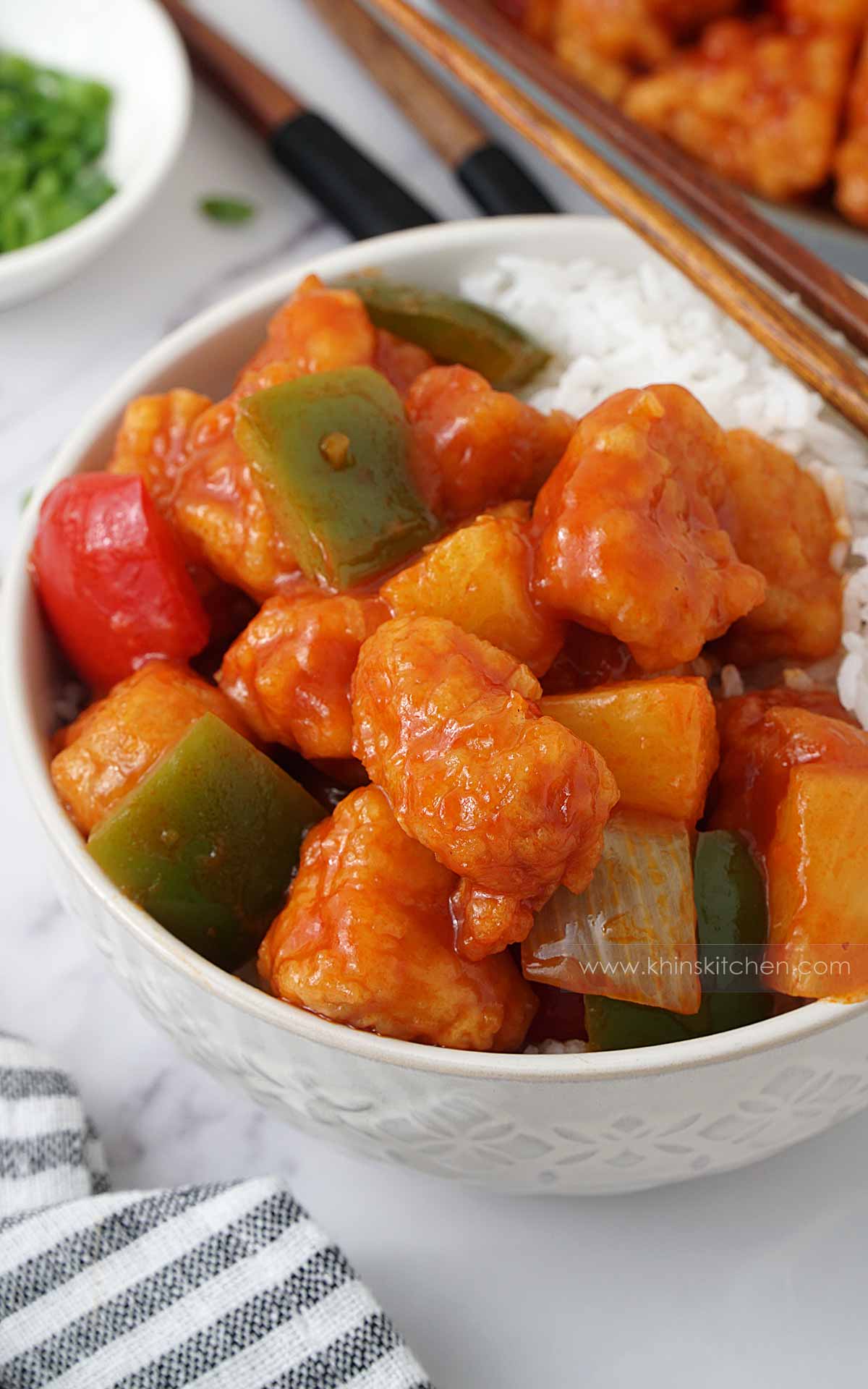 A white bowl containing fried chicken pieces and vegetables with red sweet and sour sauce. 