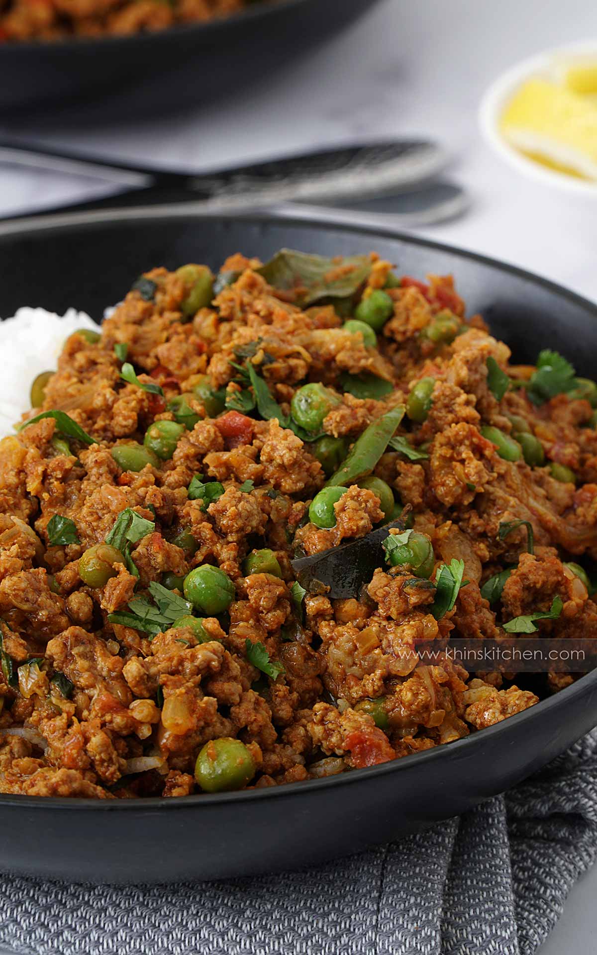 A black bowl containing, ground lamb curry with green peas, and green chillies.