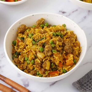 A white bowl containing fried rice with lamb mince, carrot and greenpeas.