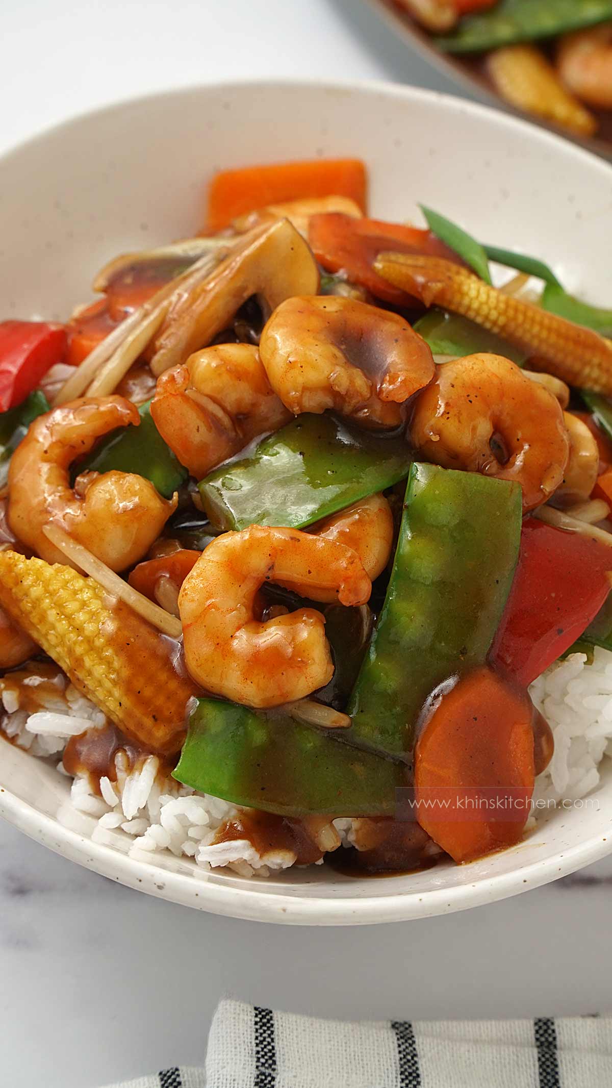 A white bowl containing rice, shrimp and vegetables with chop suey sauce. 
