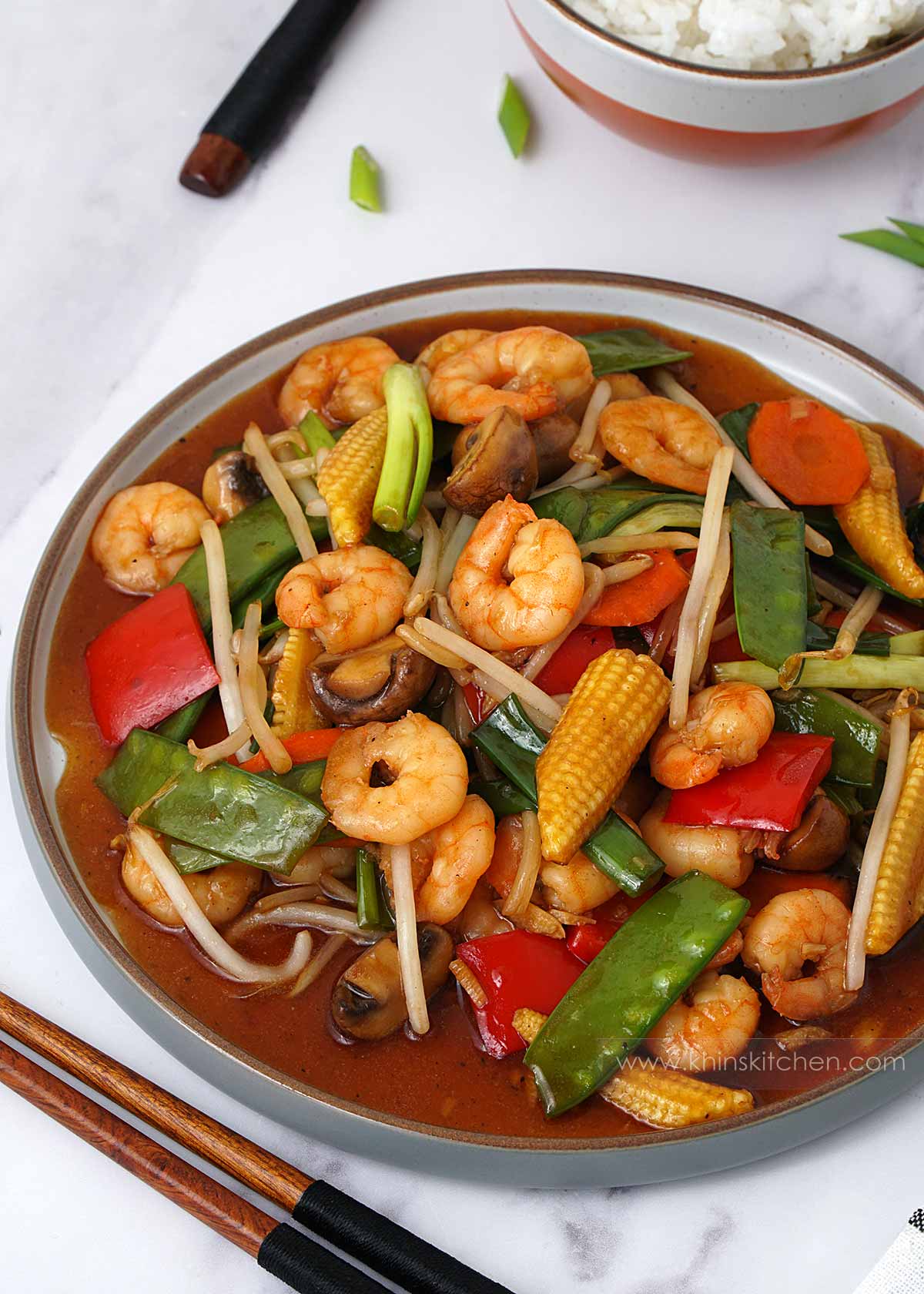 A grey plate containing prawn chop suey with king prawns and vegetables with brown sauce. 