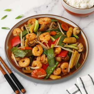 A grey plate containing stir fry king prawns and vegetables with chop suey sauce.