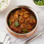A steel bowl containing prawn curry, cube bell pepper and sprinkle with coriander.