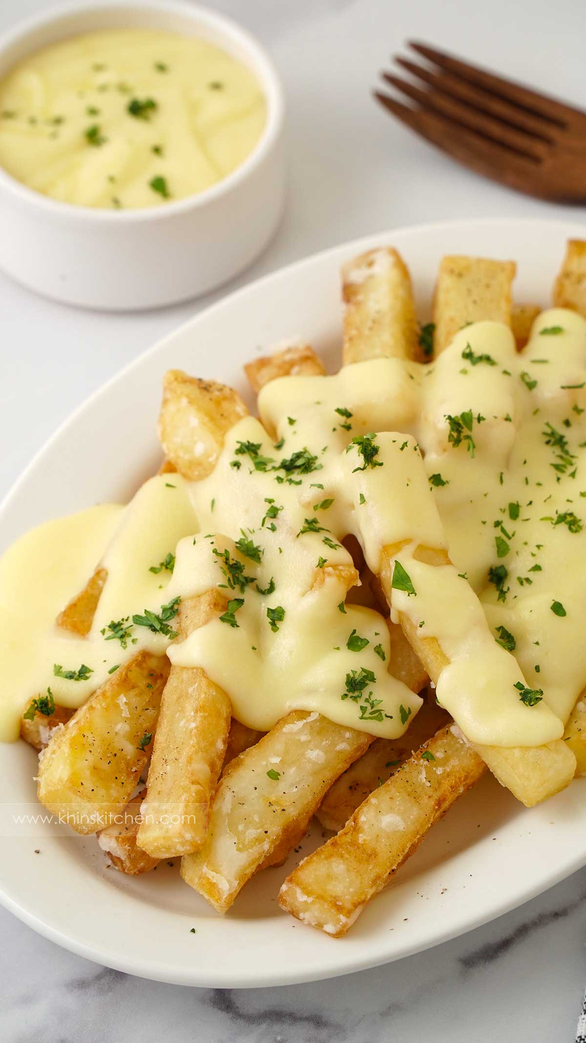 A white plate containing fried homemade cheesy chips and chopped parsley.