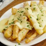 A white plate containing, fried chips topped with cheese sauce and chopped parsley.