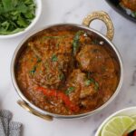 A steel metal bowl with handles, containing lamb curry with coriander and green chillies.