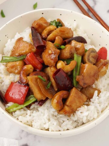 A white bowl containing spicy chicken stir fries, mushrooms, chillies and cashew nuts.