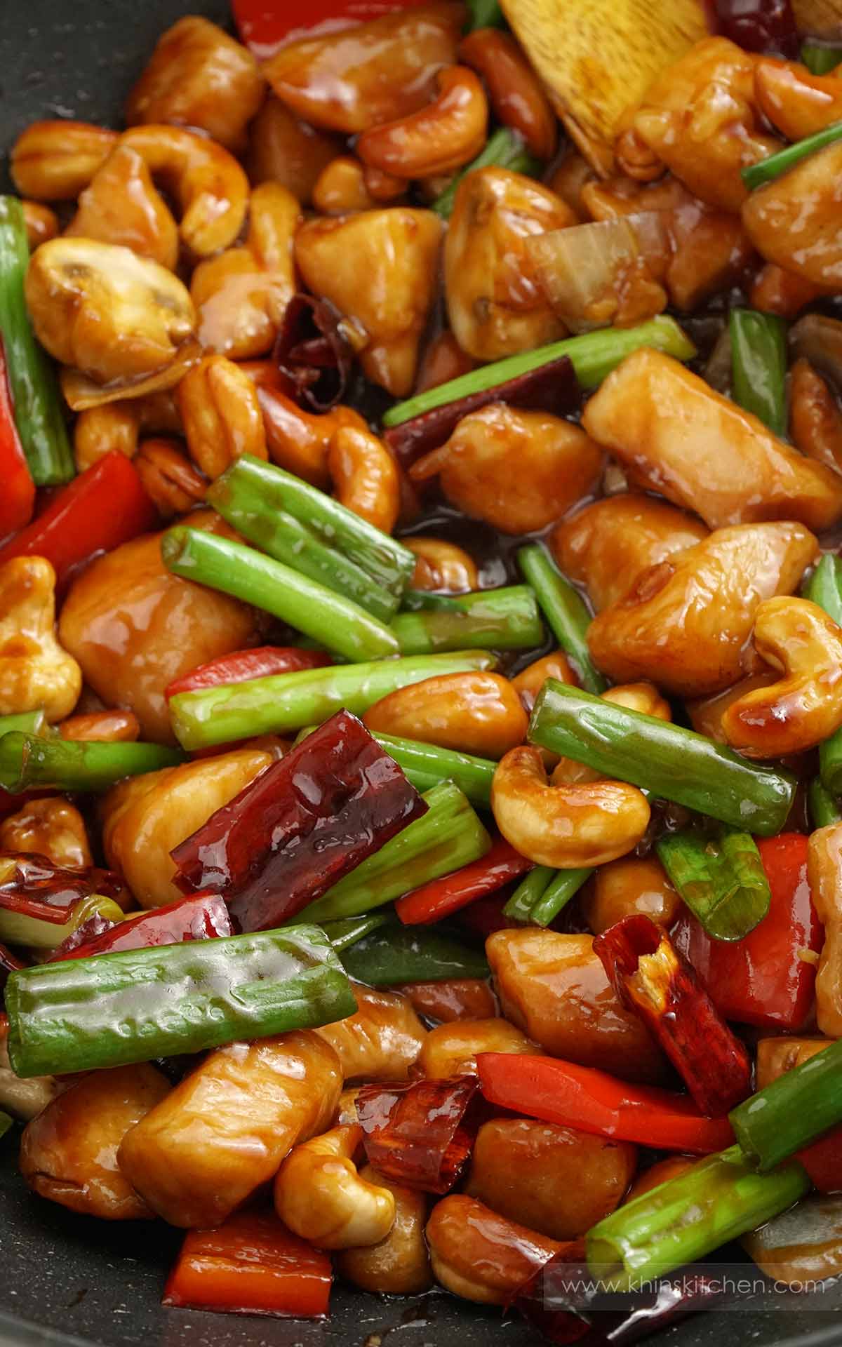 A large wok containing spicy chicken stir fries with spring onions, chillies, mushrooms and cashew nuts.