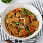A white plate containing chicken stir fry with spring onions, ginger and chilli.