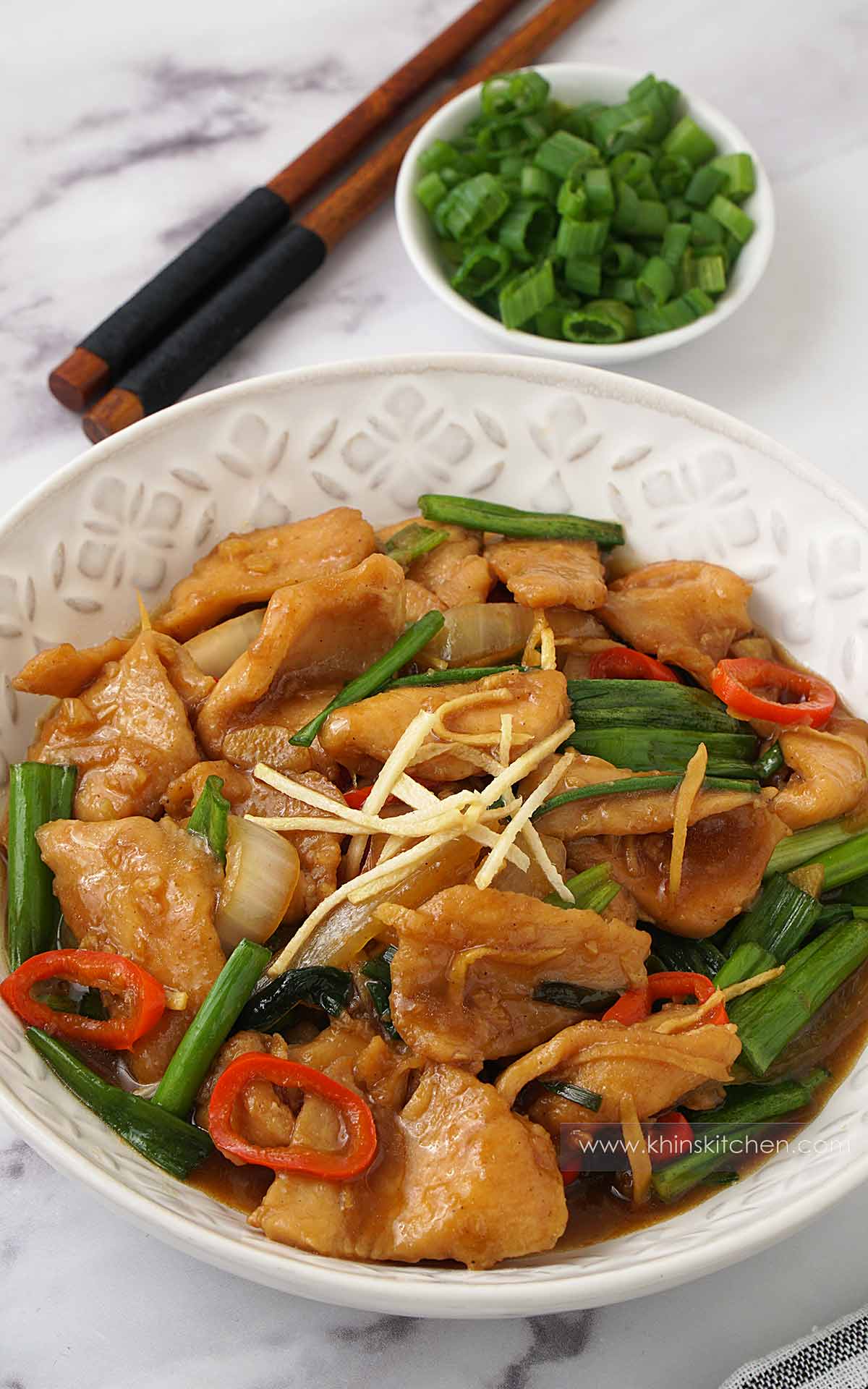 A white plate containing stir fry chicken, stir fried vegetables, sliced ginger and spring onions. 