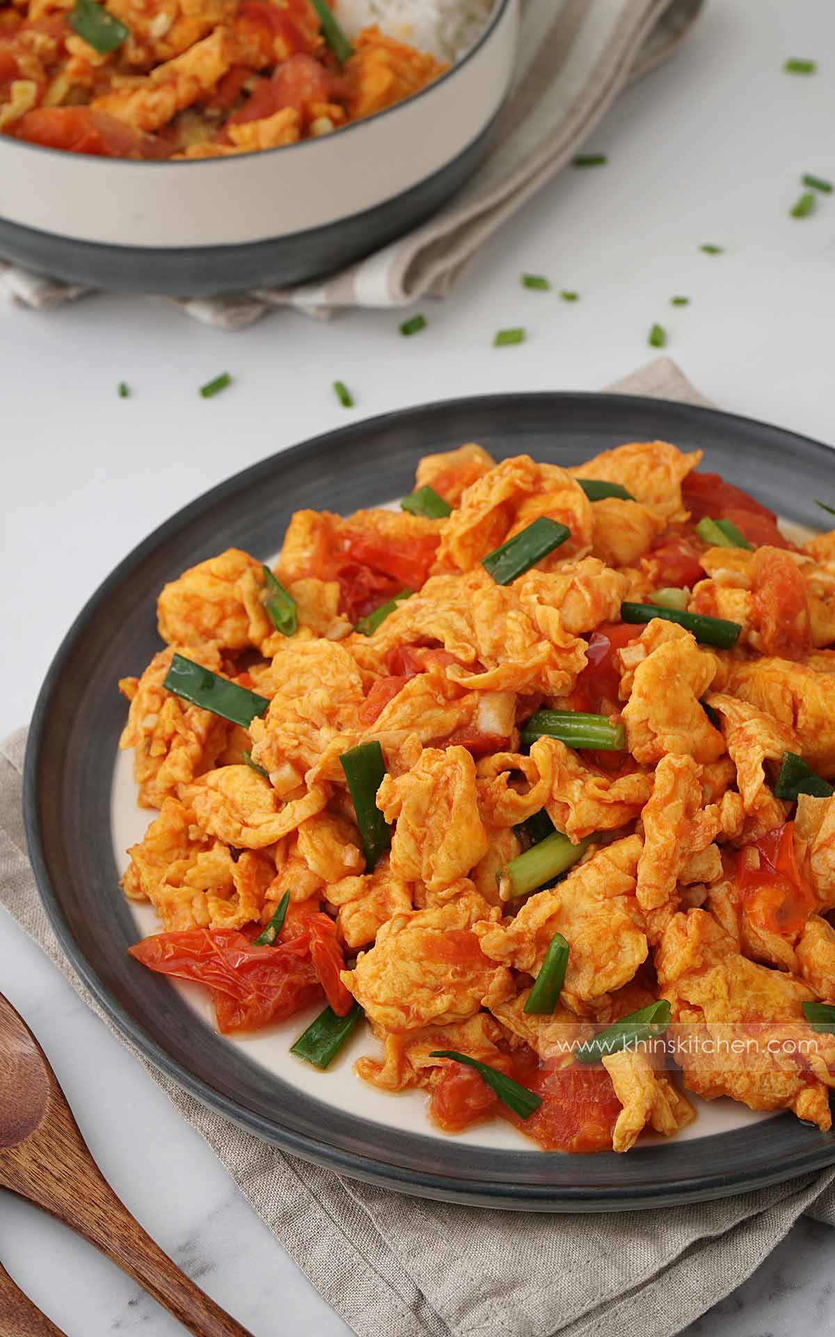 A grey plate containing golden colour egg and tomato stir fry with green onions.