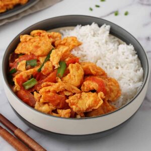 A grey bowl containing white rice, stir fried tomato and egg with spring onions.