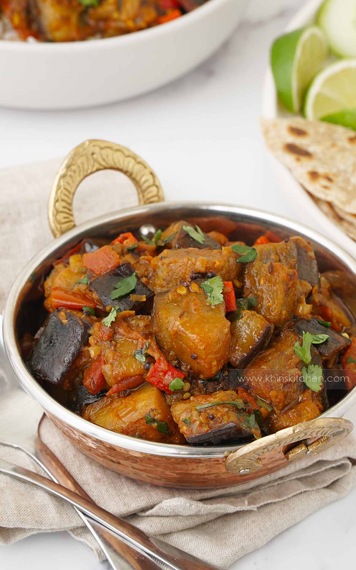 A metal serving bowl containing, eggplant dices with curry sauce.