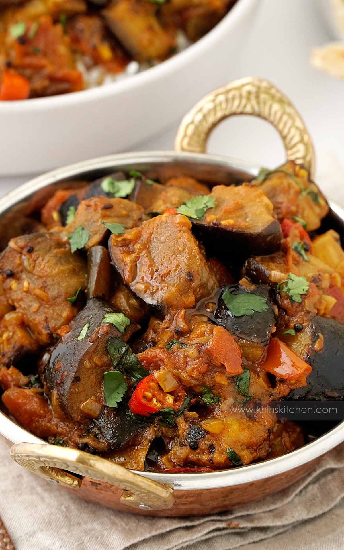 A metal bowl containing, Indian aubergine curry with mustard seeds, tomatoes, coriander and chillies. 