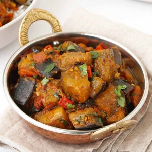 A metal bowl containing brinjal curry, garnished with coriander and fresh chillies.