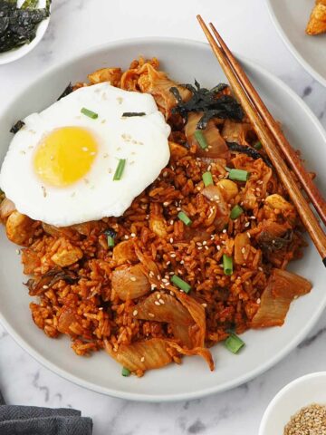 A grey plate containing Korean Bokkeumbap with kimchi, chicken, fried egg.