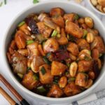 A grey bowl containing spicy chicken stir fry with peanuts, chillies, and spring onions.
