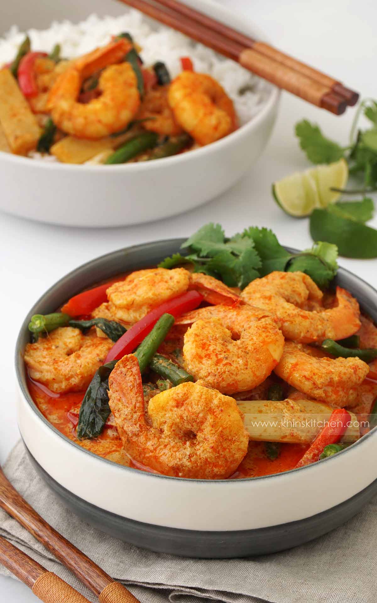 A white bowl containing, tail-on king prawns with green beans, bell peppers, coriander and creamy coconut curry sauce. 