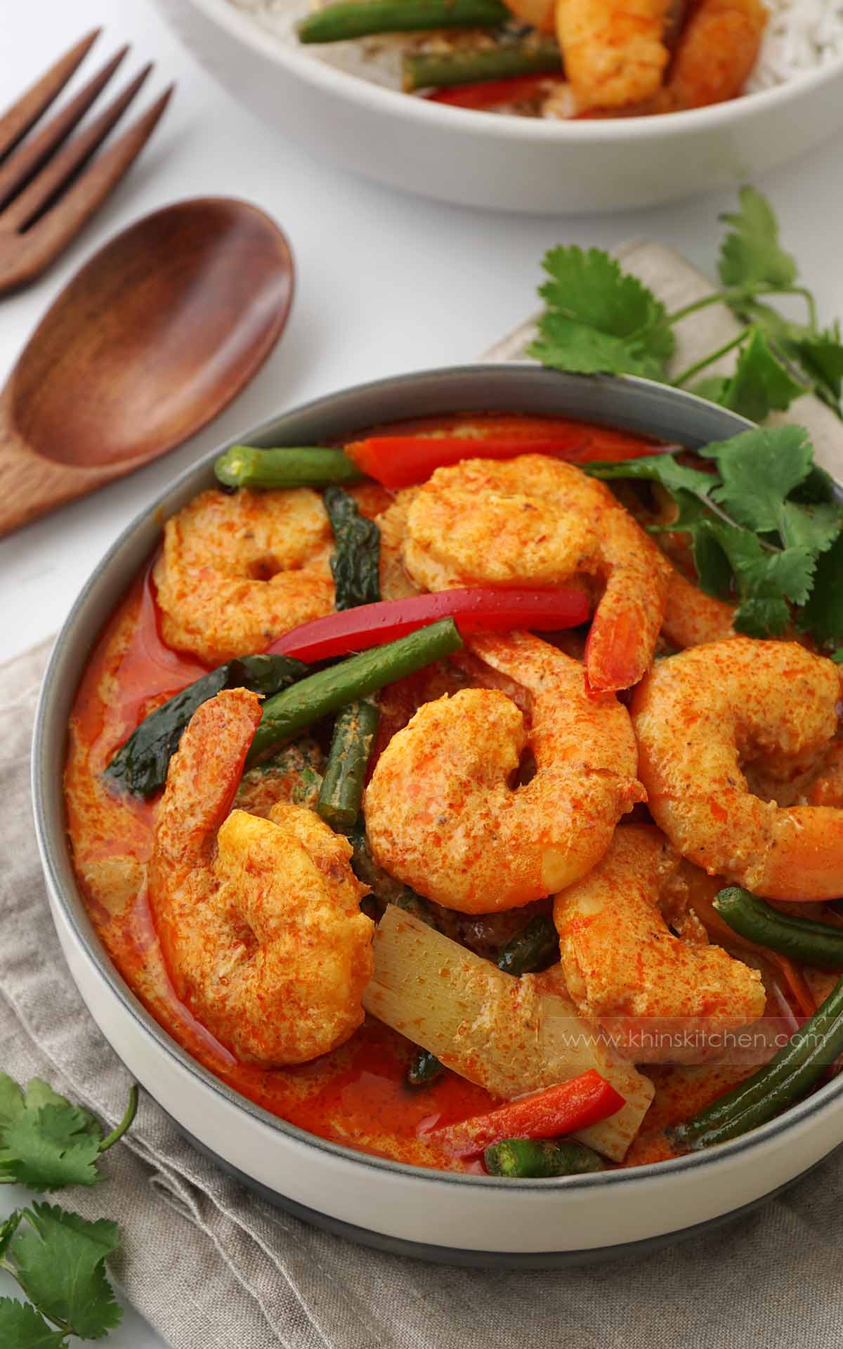 A grey bowl containing, king prawns/shrimp with vegetables and Thai red curry sauce. 