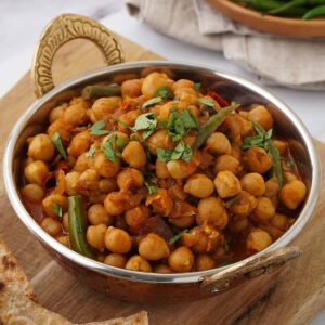 A small metal serving bowl containing chickpea curry with chopped coriander on top.