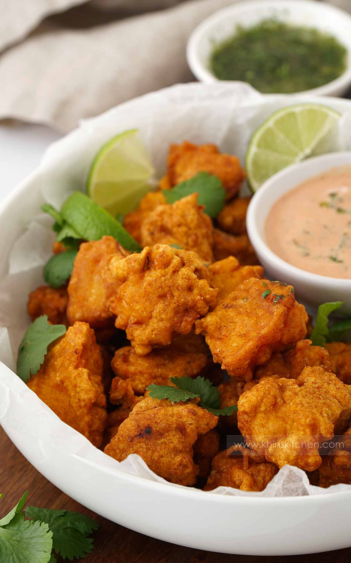 A white bowl containing, fried battered fish pieces with pakora sauce on the side. 