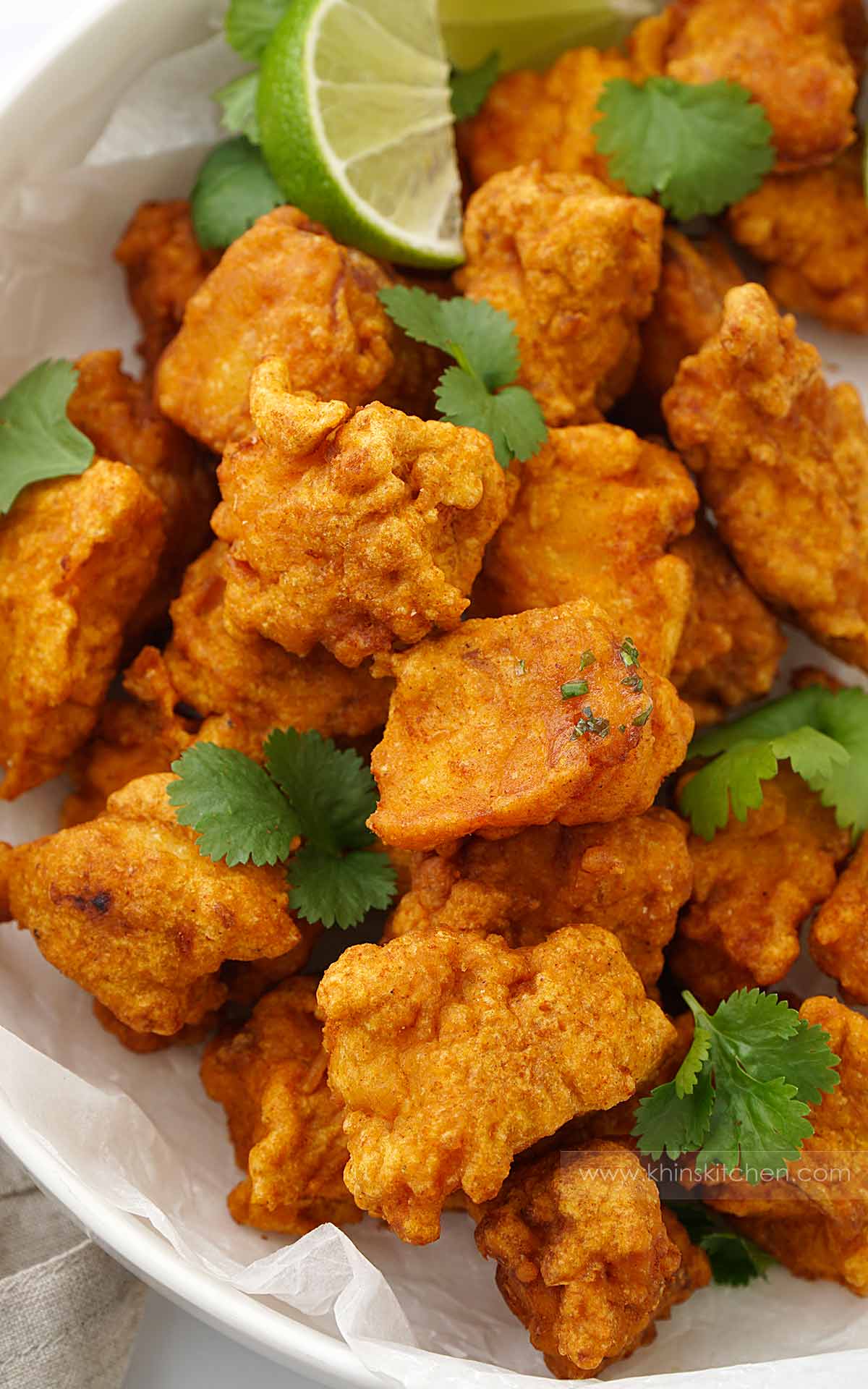 A white bowl containing crispy fried fish with coriander and lime wedges. 