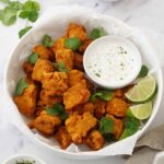 A white bowl containing, golden colour fried fish with yoghurt mint dipping sauce on the side.