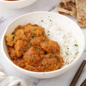 A white bowl containing, chicken masala curry and fluffy basmati rice.