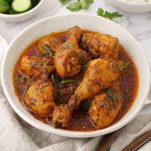 A white bowl containing bone-in chicken curry with Hyderabadi style curry sauce.