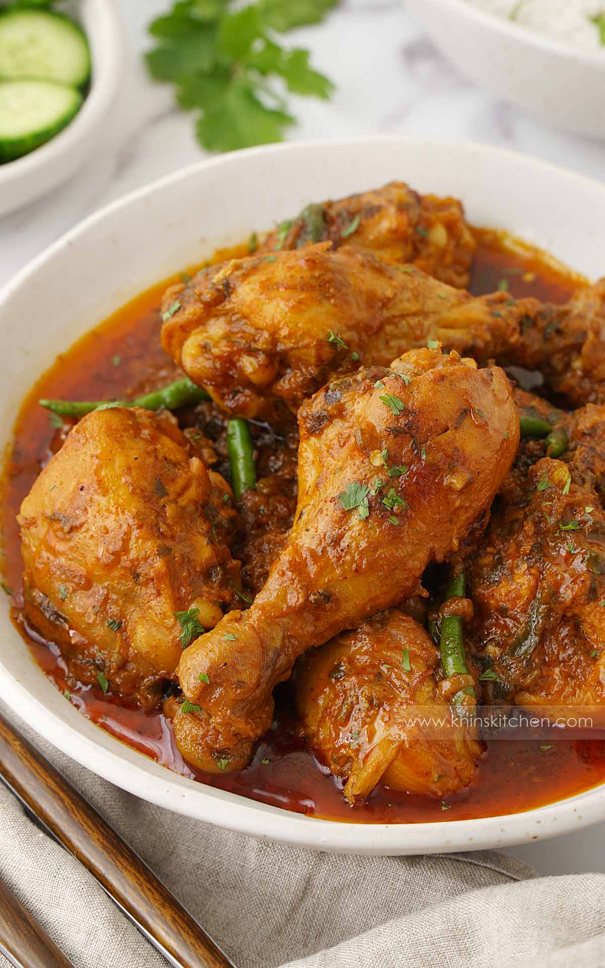 A white bowl containing, Hyderabadi style curry with bone-in chicken pieces, green chillies and chopped coriander. 