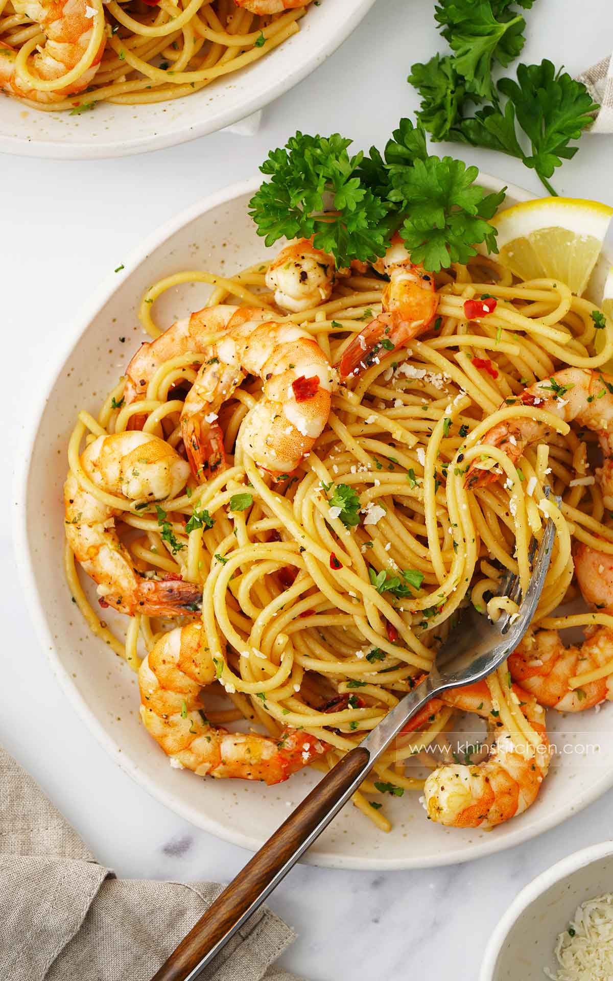 A white ceramic plate containing, spaghetti with king prawns, parsley, garlic and grated cheese. 