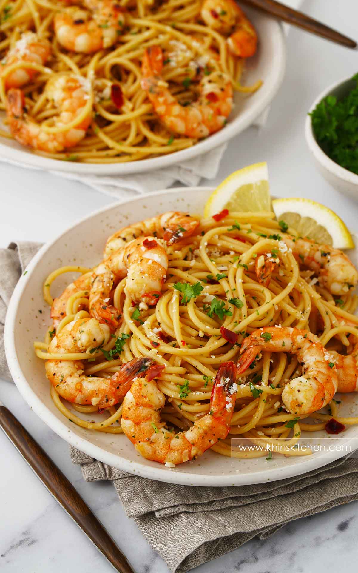 A white ceramic plate containing, spaghetti with king prawns, parsley, garlic, lemon wedges and grated cheese. 