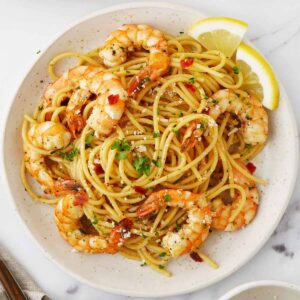 A white ceramic plate containing, spaghetti with king prawns, garlic and sprinkle with grated cheese and parsley..