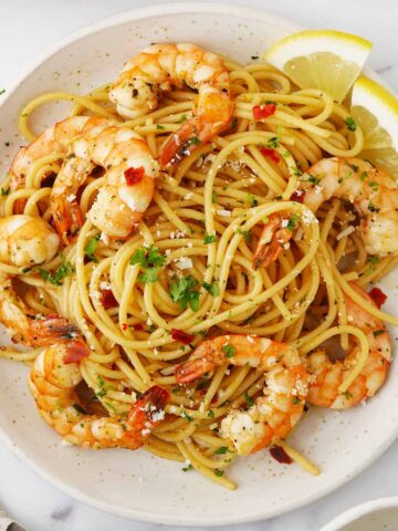 A white ceramic plate containing, spaghetti with king prawns, garlic and sprinkle with grated cheese and parsley..