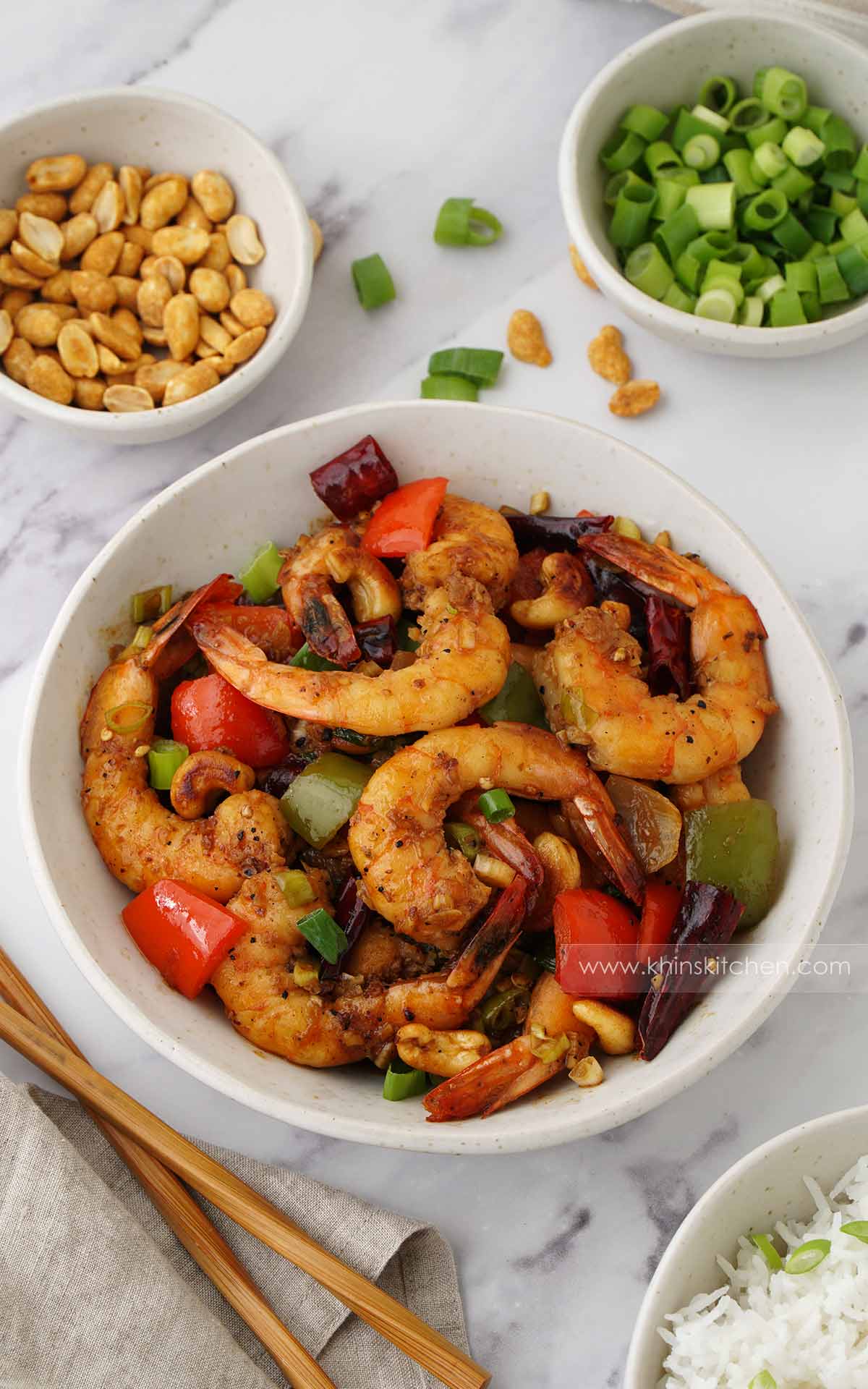 A white bowl containing Sichuan style Kung Po Prawns with crunchy cashew nuts, dried chilies and bell peppers. 