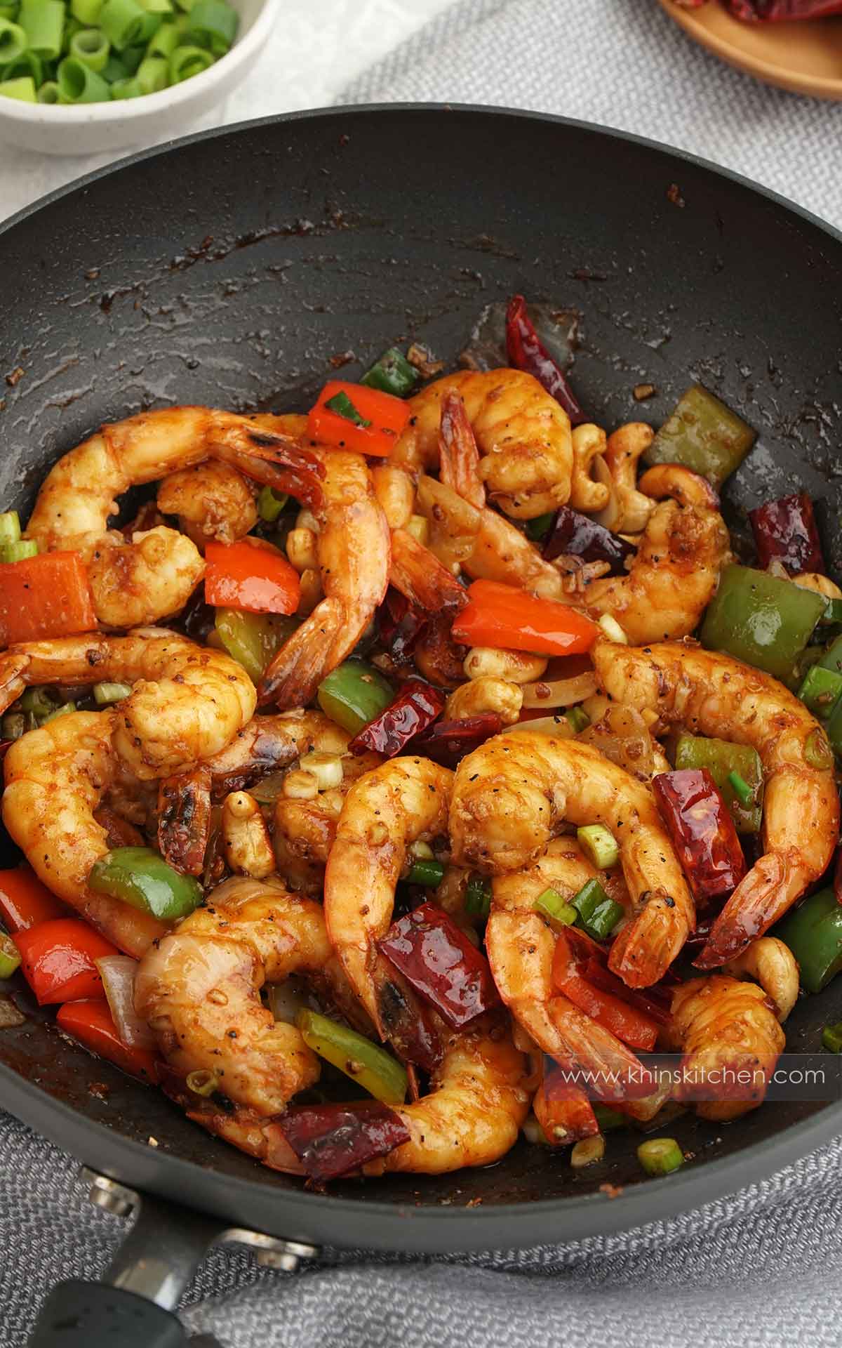 A black non-stick wok containing stir fry  shrimp with bell pepper, cashew nuts and dried chillies. 