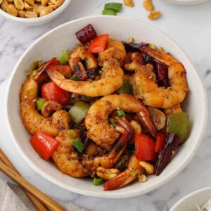 A white bowl containing, stir fried king prawns with toasted cashew nuts with spring onions and bell peppers.