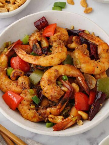 A white bowl containing, stir fried king prawns with toasted cashew nuts with spring onions and bell peppers.